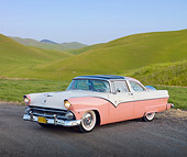 AUT 21 RK2666 01
1955 Ford Crown Victoria Pink And White 3/4 Front View On Pavement By Trees And Grassy Hills
