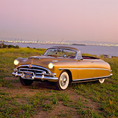 AUT 21 RK0852 02
1953 Hudson Hornet Convertible Gold 3/4 Front View On Dirt Headlights On By Water At Dusk