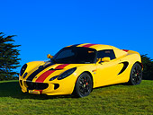 AUT 04 RK0149 03
2005 Lotus Elise Yellow Sunburst Red And Black Stripes Front 3/4 View On Grass Blue Sky