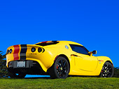 AUT 04 RK0151 01
2005 Lotus Elise Yellow Sunburst Red And Black Stripes Rear 3/4 View On Grass Blue Sky