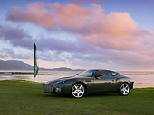 AUT 06 RK0100 01
2003 Aston Martin DB7 Zagato Green 3/4 Front View On Grass By Flag Water Sky Mountains