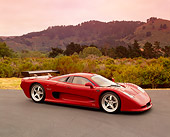 AUT 09 RK0664 01
2003 Mosler MT900S Prototype Rosa Barchetta 3/4 Front View On Pavement Bushes Background