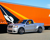 AUT 09 RK0674 04
Ford F-150 Lightning Concept Truck Silver 3/4 Side View On Pavement By Orange Semi Truck