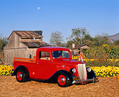 AUT 14 RK0317 07
1935 Ford 1/2 Ton Pick Up Truck Red Low 3/4 Side View By Flowers And Old Barn Blue Sky