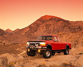 AUT 14 RK0273 01
1995 Ford F250 4x4 Red 3/4 Front View On Dirt Headlights On Hills Background Red Sky At Dusk