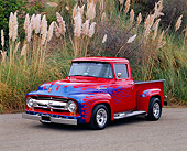 AUT 14 RK0451 02
1956 Ford F100 Pickup Truck Red With Blue Flames Front 3/4 View On Pavement By Tall Bushes