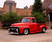 AUT 14 RK0521 01
1955 Ford F-100 Custom Pick Up Truck Red 3/4 Side View On Pavement By Building And Trees