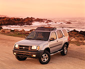AUT 15 RK0181 05
2000 Nissan Xterra SE Silver Overhead 3/4 Front View On Sand By Ocean And Rocks Headlights On Light Orange Sky