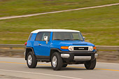 AUT 15 RK0964 01
2007 Toyota FJ Cruiser Blue And White 3/4 Front View On Road By Grass Hills