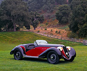 AUT 19 RK0098 02
1939 Red And Black Alfa Romeo 6C 2500 Super Sport 3/4 Front On Grass By Fence And Trees Headlights On