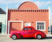 AUT 19 RK0186 02
1939 Ford Coupe Red With Flames Hot Rod Profile View By Old Building