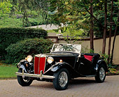 AUT 21 RK0286 02
1952 Black MG TD Convertible 3/4 Front View On Pavement Headlights On By Trees And Bushes