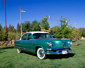 AUT 21 RK1567 02
1953 Kaiser Dragon Green White Top 3/4 Front View On Grass By Trees Flag Poles Blue Sky