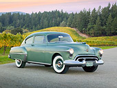 AUT 21 RK3214 01
1950 Oldsmobile Futuramic 88 Club Sedan Moss Green 3/4 Front View On Pavement By Vineyard And Evergreen Trees