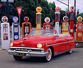 AUT 21 RK0280 02
1951 Red Lincoln Convertible Cosmopolitan 3/4 Front View By Different Old Gas Pumps Headlights On At Dusk