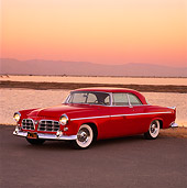 AUT 21 RK0617 02
1955 Chrysler C-300 Red 3/4 Front View On Pavement By Water Headlights On Orange Sky
