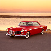 AUT 21 RK0617 11
1955 Chrysler C-300 Red 3/4 Front View On Pavement By Water Headlights On Orange Sky