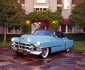 AUT 21 RK0684 03
1953 El Dorado Cadillac Light Blue 3/4 Front View On Driveway Headlights On By House And Trees At Dusk