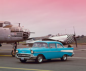AUT 21 RK0845 07
1957 Chevy 210 Blue And White 3/4 Side View On Pavement By Airplanes Headlights On Orange Sky