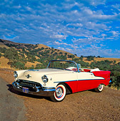 AUT 21 RK0876 02
1955 Olds Super 88 Red And White Convertible 3/4 Side View On Dirt Hills Cloudy Blue Sky