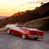 AUT 21 RK0880 03
1955 Olds Super 88 Red And White Convertible 3/4 Rear View On Dirt By Hill Orange Sky At Dusk