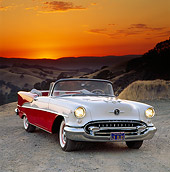 AUT 21 RK0883 07
1955 Oldsmobile Super 88 Red And White Convertible 3/4 Front View On Gravel Sunset Background Orange Sky