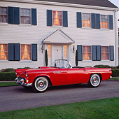 AUT 21 RK0889 03
1955 Ford Thunderbird Red Side 3/4 View On Pavement In Front Of House Parking Lights On At Dusk