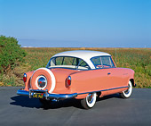 AUT 21 RK1391 02
1955 AMC Nash Rambler Country Club Pink 3/4 Rear View On Pavement By Tall Grass Blue Sky