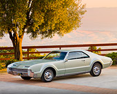 AUT 22 BK0046 01
1966 Oldsmobile Toronado Green Silver 3/4 Front View On Pavement By Tree And Fence