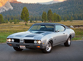AUT 22 RK3412 01
1969 Oldsmobile 442 Gray With Black Stripes 3/4 Front View On Pavement By Evergreen Trees And Mountains