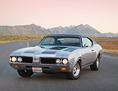 AUT 22 RK3413 01
1969 Oldsmobile 442 Gray With Black Stripes 3/4 Front View On Road By Mountains At Dusk