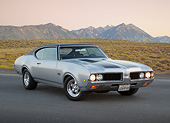 AUT 22 RK3414 01
1969 Oldsmobile 442 Gray With Black Stripes 3/4 Front View On Pavement By Mountains At Dusk
