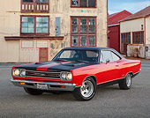 AUT 22 RK3445 01
1969 Plymouth GTX Red With Black Stripes 3/4 Front View On Pavement By Old Factory Building