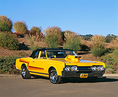 AUT 22 RK0951 02
1967 Oldsmobile Cutlass Yellow 3/4 Front View On Pavement By Bushes Blue Sky