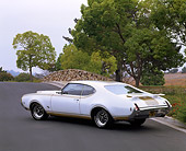 AUT 22 RK0956 02
1969 Oldsmobile Hurst 455 White And Gold 3/4 Rear View On Pavement By Trees
