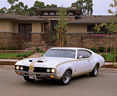 AUT 22 RK0961 02
1969 Hurst Oldsmobile 455 White And Gold 3/4 Front View On Pavement By House