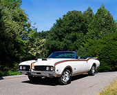 AUT 22 RK1490 02
1969 Oldsmobile Hurst Convertible White Gold Stripe Low 3/4 Front View On Pavement By Trees