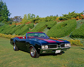 AUT 22 RK1820 02
1969 Oldsmobile 442 Convertible Red And Black 3/4 Front View On Grass By Shrubs