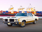 AUT 23 RK2080 01
1972 Hurst Oldsmobile Cutlass White And Gold 3/4 Front View On Pavement By Shipping Yard