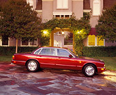 AUT 25 RK0457 02
1995 Red XJ6 Jaguar Side View On Driveway In Front Of House Headlights On At Dusk