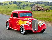 AUT 26 RK3243 01
1934 Chevrolet 3-Window Coupe Red With Flames 3/4 Front View On Road By Grassy Hills And Old Shed