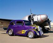 AUT 26 RK0270 03
1951 Ford Anglia Purple With Flames 3/4 Front View On Pavement By Military Airplane Blue Sky