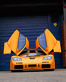 AUT 28 RK0064 02
1996 McLaren F1 LM Orange Head On Doors Open On Pavement By Blue Garage Door