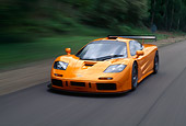 AUT 29 RK0124 15
1996 McLaren F1 LM Orange In Motion 3/4 Front View On Road By Grass And Trees