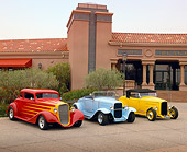 AUT 31 RK0114 01
Chevrolet 5 Window Coupe Red With Flames And 1930s Ford Roadsters Blue And Yellow 3/4 Front View On Pavement By Building