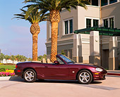 AUT 33 RK0162 02
2000 Mazda Miata Convertible Mahogany 3/4 Side View On Pavement By Palm Tree And Building