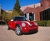 AUT 35 RK0292 01
2002 Mini Cooper S Red With White Stripes Low 3/4 Front View On Pavement By Museum And Trees Blue Sky