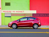 AUT 46 BK0025 01
2011 Ford Fiesta Red Profile View On Road By Green And Red Building