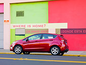 AUT 46 BK0026 01
2011 Ford Fiesta Red Profile View On Road By Green And Red Building