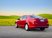 AUT 46 BK0047 01
2011 Ford Fusion Hybrid Red 3/4 Rear View On Pavement By Field Of Wildflowers